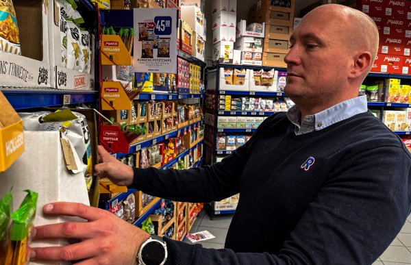 Mann med Rema 1000-uniform rydder i hyllene i butikken.