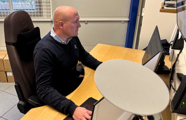 Mann i Rema 1000-uniform sitter på kontoret foran pcen.