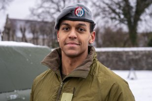 Mann ikledd militære klær og beret og smiler. Bak han skimter man en militærbil.