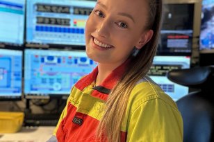 Ei dame i arbeidsklær. Hun har langt og lyst hår. Hun sitter foran flere skjermer. Hun jobber på en flyterigg.