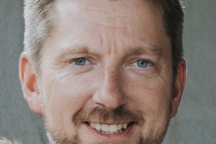 En mann med kort hår og skjegg. Han smiler og ser rett i kameraet.