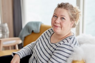 Portrettbilde av Miriam Johansen i en stol med skinn. Hun er iført stripete genser og har blondt hår. I bakgrunnen ser man et vindu ut mot sjøen.