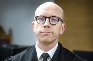 Mann i svart kappe, hvit skjorte, slips og briller