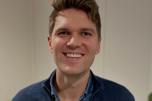 Portrettbilde av en mann med brunt hår og blå skjorte. I bakgrunnen er en lys vegg.