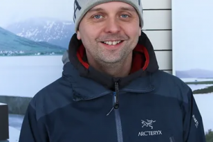 En mann i mørke klær. Han smiler og ser rett i kameraet. 