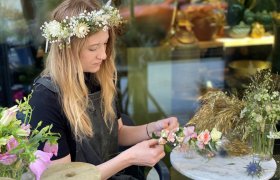 Blomsterdekoratør Ingrid Marie Aarre med blomsterkrans i håret lager en blomsterkrans med rosa blomster