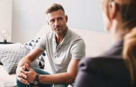 Voksen mann sitter i en sofa og lytter til en kvinne
