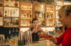 En kvinnelig bartender lager en drink til en gjest på baren