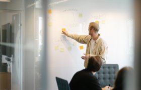 En mannlig markedssjef peker på en post-it lapp på et whiteboard.