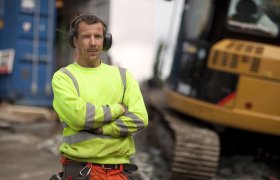 Ein anleggsmaskinfører står ved gravemaskinen sin.