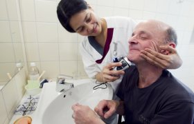 Helsefagarbeidar som hjelper ein mannleg pasient med barberingen.