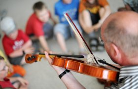 Musikkpedagog underviser elevene i å spille fiolin.
