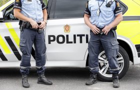 To politimenn står foran en politibil.