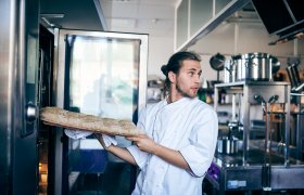 Ung mannlig baker setter bakverk i ovnen