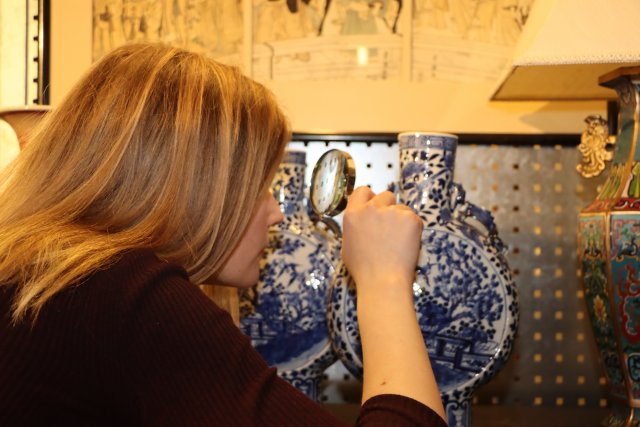 En kvinne studerer en asiatisk vase gjennom et forstørrelsesglass.