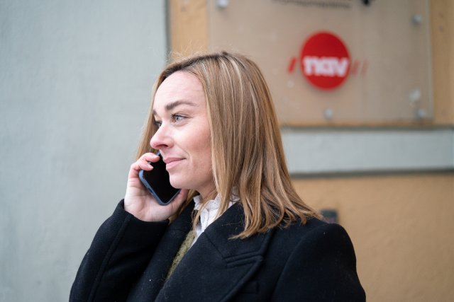 En kvinne i telefonsamtale med et NAV-skilt i bakgrunnen.