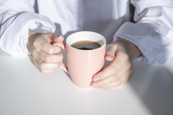 Bilde av hender som holder en kaffekopp i solskinn.