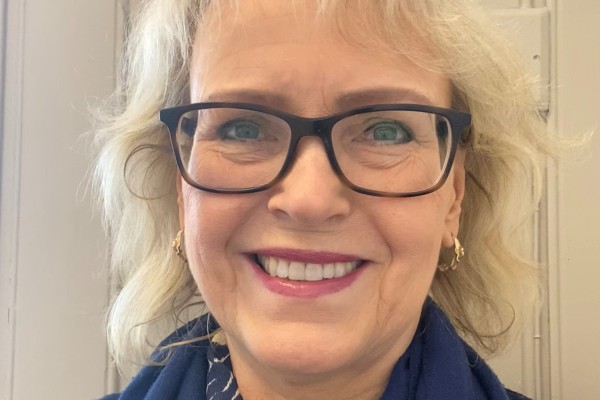 Portrettbilde av blond, smilende dame med briller