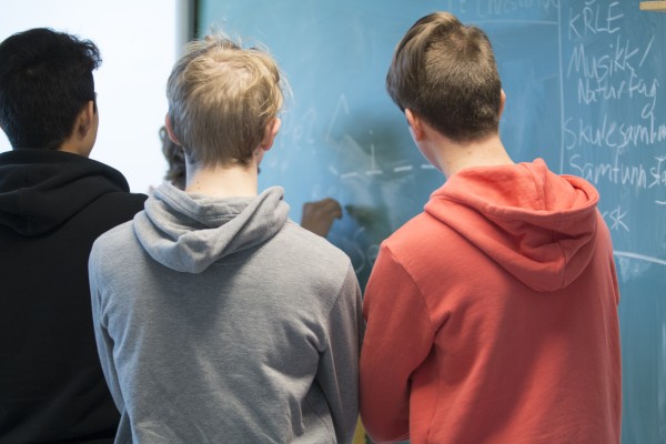 Bilde av tre gutter som står foran en tavle